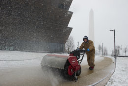 The Washington Monument is seen in the background as a worker clears snow from a sidewalk at the National Museum of African American History and Culture during a Spring snowstorm in Washington, Wednesday, March 21, 2018. (AP Photo/Cliff Owen)