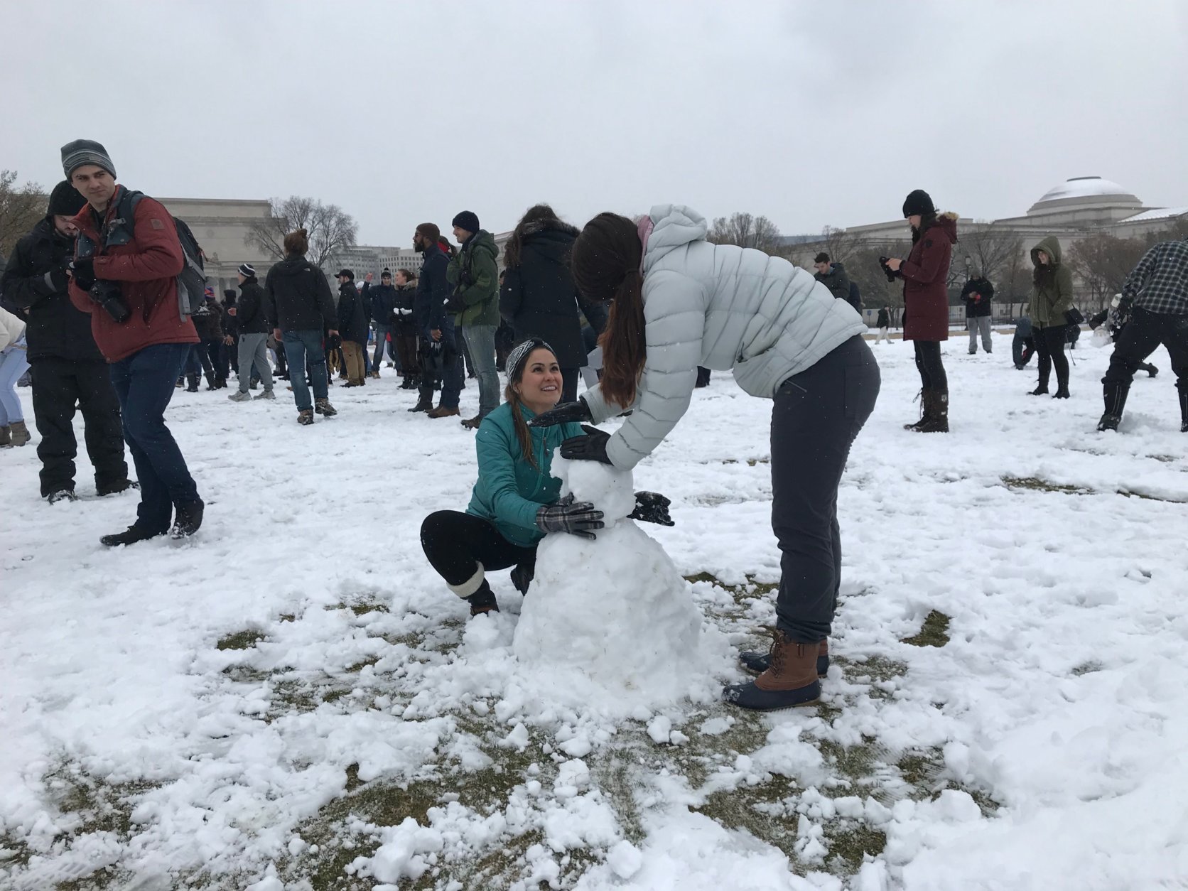 Two people make a snowman with the the thin layer of snow that fell on the National Mall on Wednesday, March 21, 2018. (WTOP/Dick Uliano)