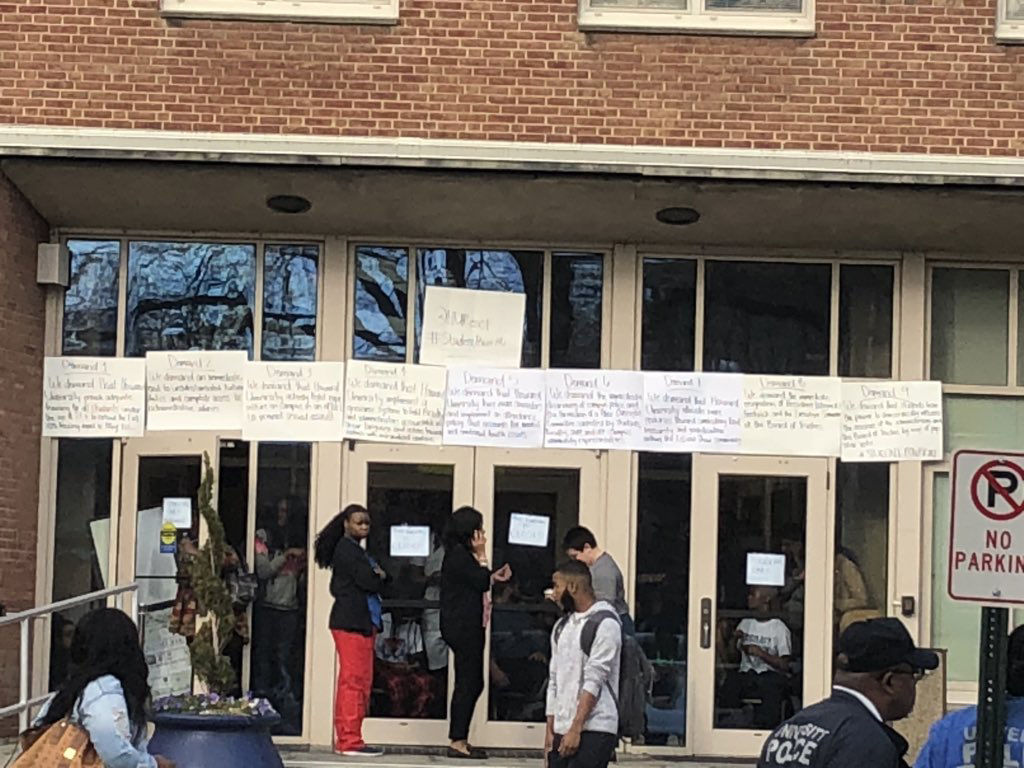 People linger outside the administration building on the campus of Howard University. Students have been holding a sit-in in the building since Thursday night with their demands posted outside. (WTOP/Melissa Howell)