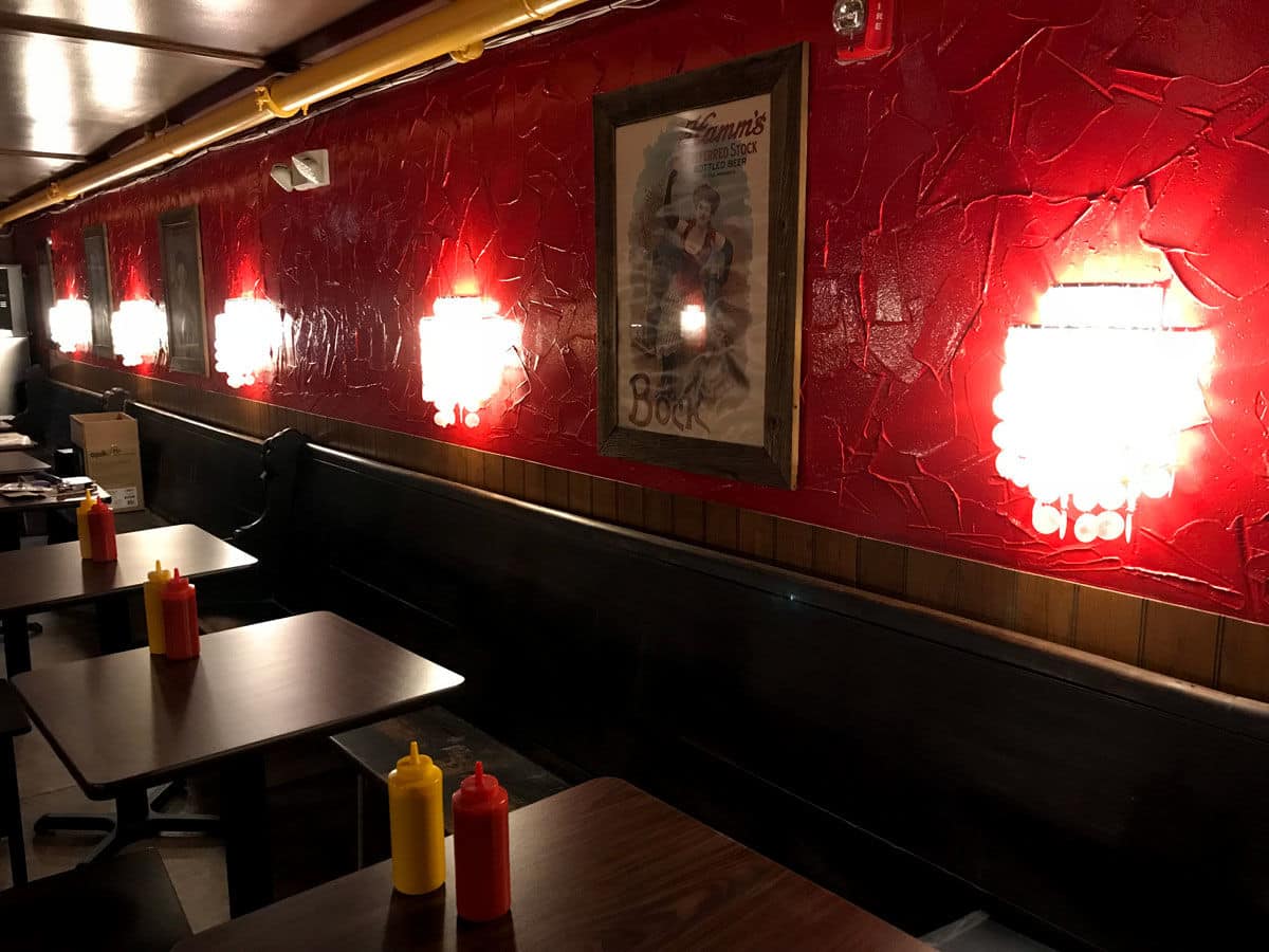 In one part of the Quarry House Tavern, the red walls familiar to regulars are back, along with capiz shell wall sconces, vintage beer posters and church pew seating. (WTOP/Michelle Basch)