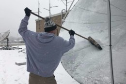 WTOP's Chris Cichon clearing snow off the satellite dish atop the Glass Enclosed Nerve Center. (WTOP/Max Smith)