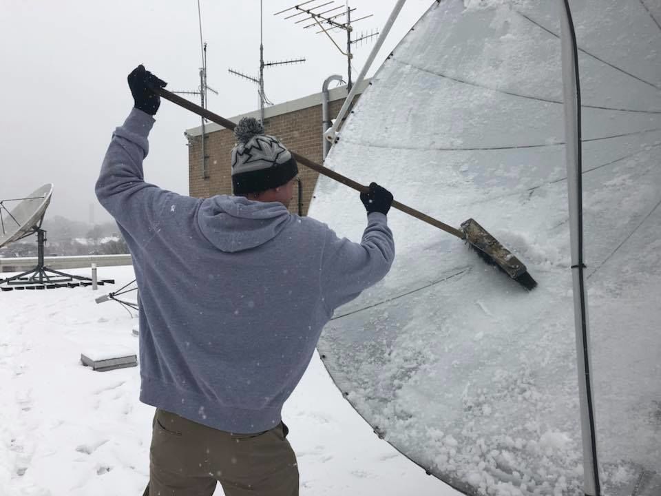 WTOP's Chris Cichon clearing snow off the satellite dish atop the Glass Enclosed Nerve Center. (WTOP/Max Smith)