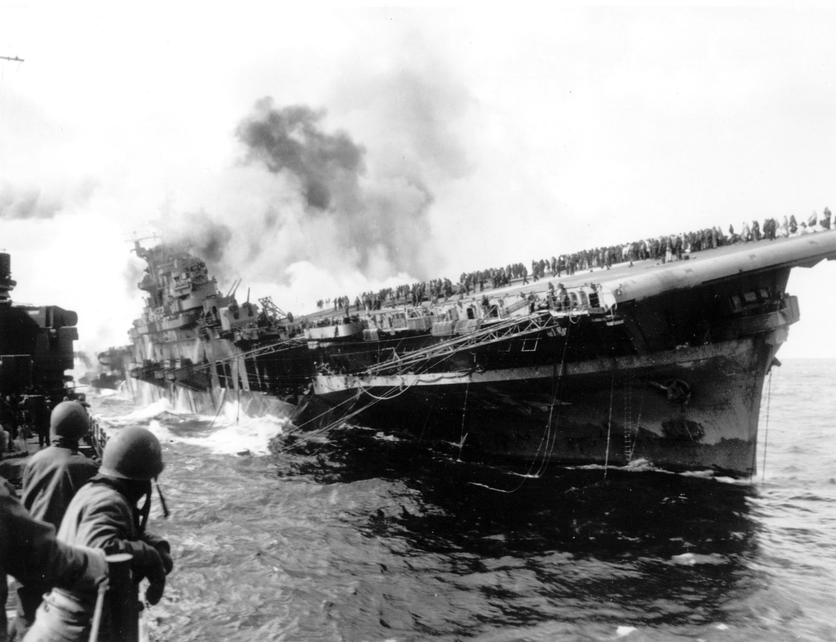 In this image provided by the U.S. Navy, the USS Santa Fe lies alongside the heavily listing USS Franklin to provide assistance after the aircraft carrier had been hit and set afire by a single Japanese dive bomber, during the Okinawa invasion, on March 19, 1945, off the coast of Honshu, Japan.  (AP Photo/U.S. Navy)