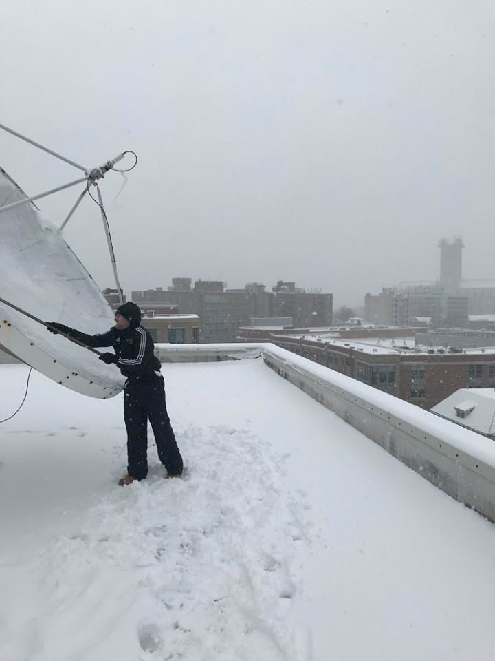 WTOP's Max Smith taking his turn to clear snow off the satellite dish atop the WTOP studio in NW. (WTOP/Chris Cichon)