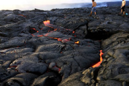 In this Monday, Aug. 8, 2016 photo, lava from Kilauea, an active volcano on Hawaii's Big Island, flows toward the ocean in Volcanoes National Park near Kalapana, Hawaii. The current lava flow erupted from a vent on the volcano in May and made its way to the sea in late July. Visitors can hike about 10 miles round trip to see the lava, or take a boat or helicopter tour to see the flow. (AP Photo/Caleb Jones)