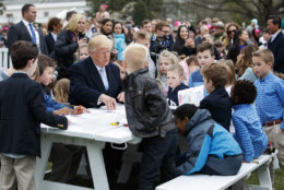 President Donald Trump sits with children writing cards for troops at the White House in Washington, Monday, April 2, 2018, during the annual White House Easter Egg Roll. (AP Photo/Carolyn Kaster)