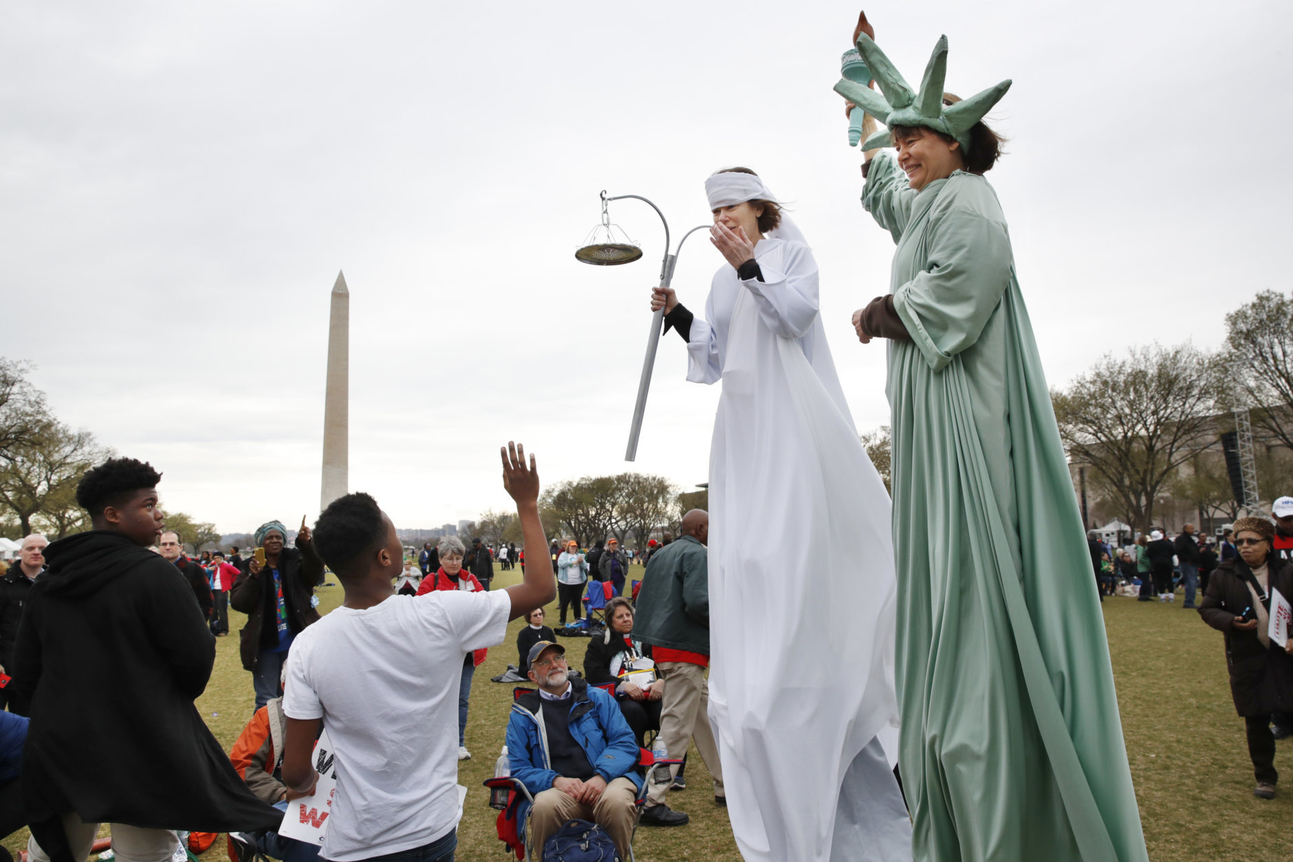 Eric McLaughlin, 14, left, and his cousin Markale McLean, 13, both of Washington, wave to Carolyn McCarthy, dressed on stilts as "Lady Justice," and Debbie Davis, dressed as "Lady Liberty," both of Milwaukee, Wisc., as they attend the A.C.T. To End Racism rally, Wednesday, April 4, 2018, on the National Mall in Washington, on the 50th anniversary of Martin Luther King Jr.'s assassination. (AP Photo/Jacquelyn Martin)