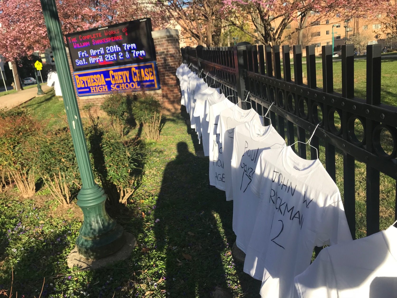 T-shirts, each inscribed with the name and age of a 2018 gun violence victim hangs on the fence, along busy East-West Highway. (WTOP/Neal Augenstein)
