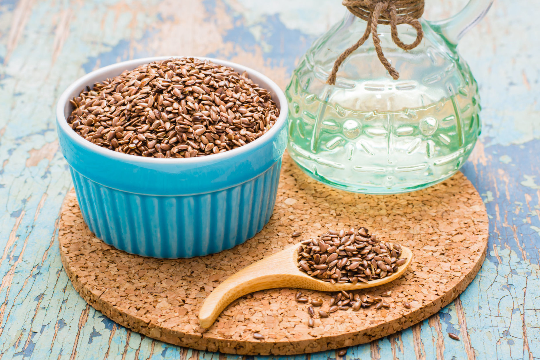 Flax seeds in a spoon and a bowl, linseed oil in a bottle on a wooden table