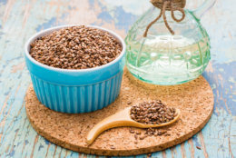 Flax seeds in a spoon and a bowl, linseed oil in a bottle on a wooden table