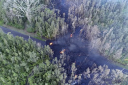 In this still frame taken from video, lava flows over a road in the Puna District as a result of the eruption from Kilauea Volcano on Hawaii's Big Island Friday, May 4, 2018. The eruption sent molten lava through forests and bubbling up from paved streets and forced the evacuation of about 1,500 people who were still out of their homes Friday after Thursday's eruption. (Byron Matthews via AP)