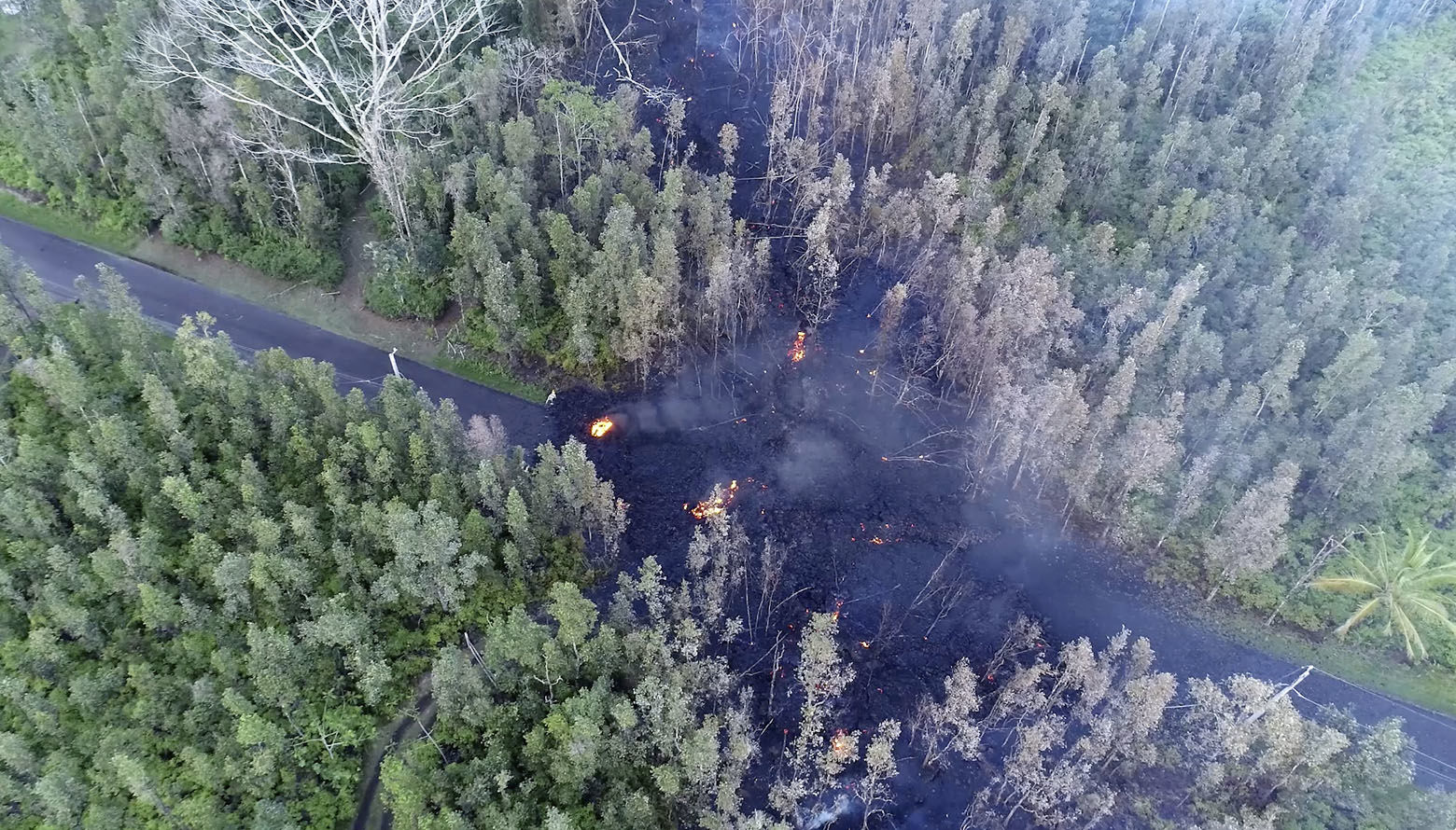 In this still frame taken from video, lava flows over a road in the Puna District as a result of the eruption from Kilauea Volcano on Hawaii's Big Island Friday, May 4, 2018. The eruption sent molten lava through forests and bubbling up from paved streets and forced the evacuation of about 1,500 people who were still out of their homes Friday after Thursday's eruption. (Byron Matthews via AP)
