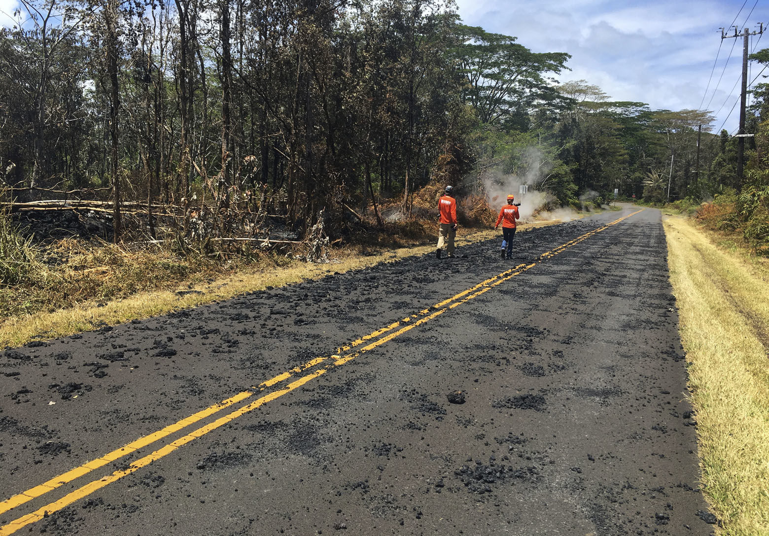 In this Sunday, May 6, 2018 photo provided by the U.S. Geological Survey, USGS scientists monitoring the eruption of Kilauea volcano in Leilani Estates walk past spatter that erupted from a fissure on Leilani Avenue,  in the Leilani Estates subdivision near Pahoa on the island of Hawaii. Kilauea volcano has destroyed more than two dozen homes since it began spewing lava hundreds of feet into the air last week, and residents who evacuated don't know how long they might be displaced. The decimated homes were in the Leilani Estates subdivision, where molten rock, toxic gas and steam have been bursting through openings in the ground created by the volcano. (U.S. Geological Survey via AP)