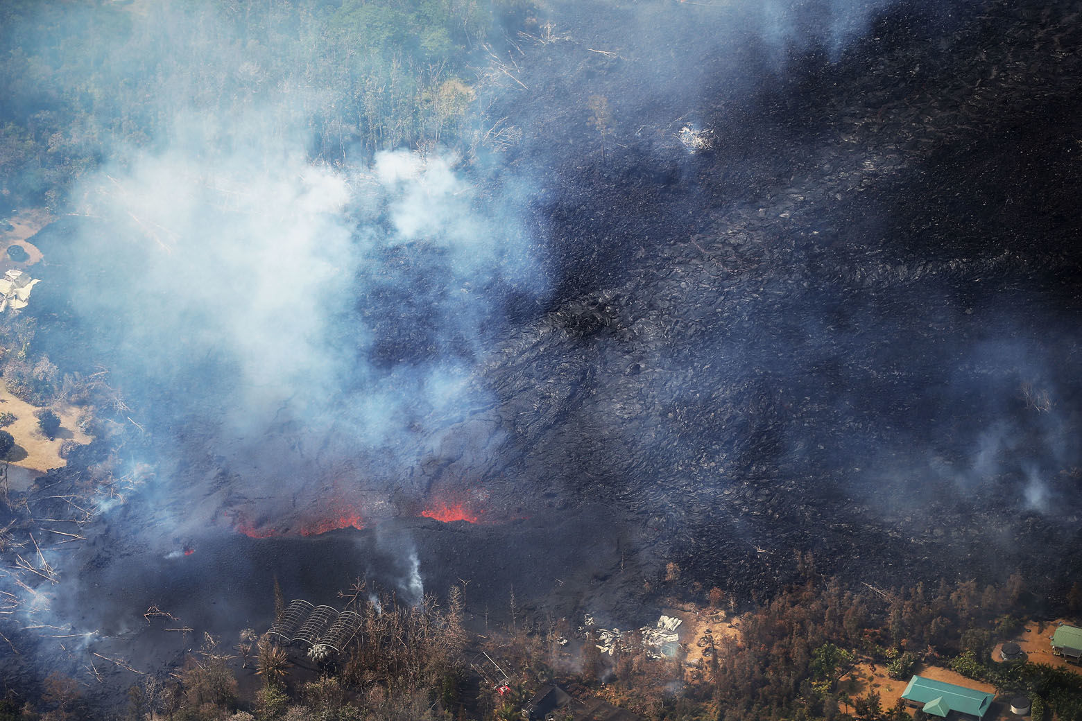 PAHOA, HI - MAY 06:  Lava from volcanic fissures slowly flows and overtakes structures and trees in the Leilani Estates neighborhood in the aftermath of eruptions from the the Kilauea volcano on Hawaii's Big Island on May 6, 2018 in Pahoa, Hawaii. A magnitude 6.9 earthquake struck the island May 4. The volcano has spewed lava and high levels of sulfur gas into communities, leading officials to order 1,700 to evacuate. Officials have confirmed 26 homes have now been destroyed by lava in Leilani Estates.  (Photo by Mario Tama/Getty Images)