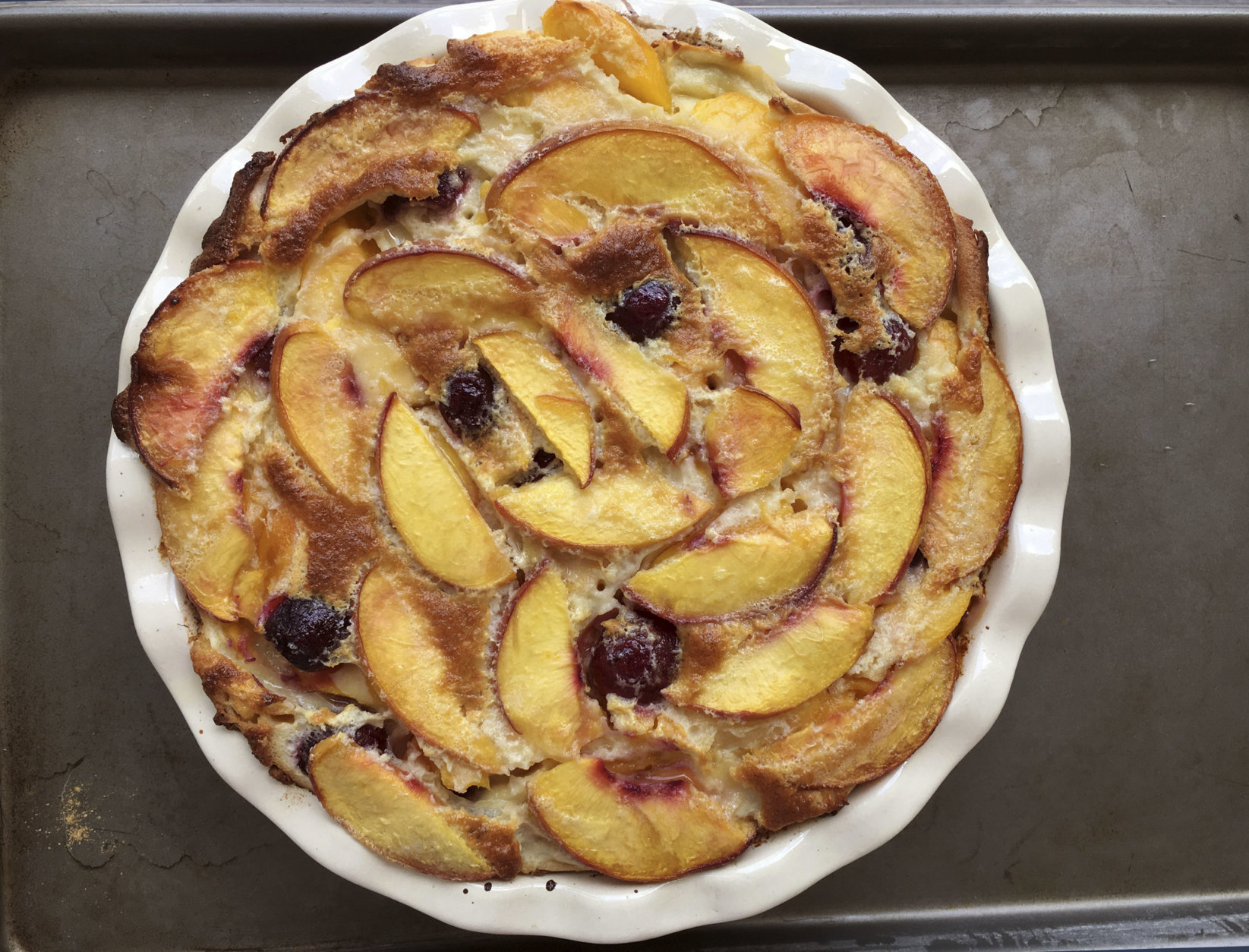 This July 22, 2017 photo shows a summer peach clafoutis in Houston, Texas. This dish is from a recipe by Elizabeth Karmel. The recipe that can be tailored to whatever summer fruit is on hand, and not just cherries, which are traditionally used in France for this rustic dessert that envelopes the fruit in a custardy crepe-like batter. (Elizabeth Karmel via AP)