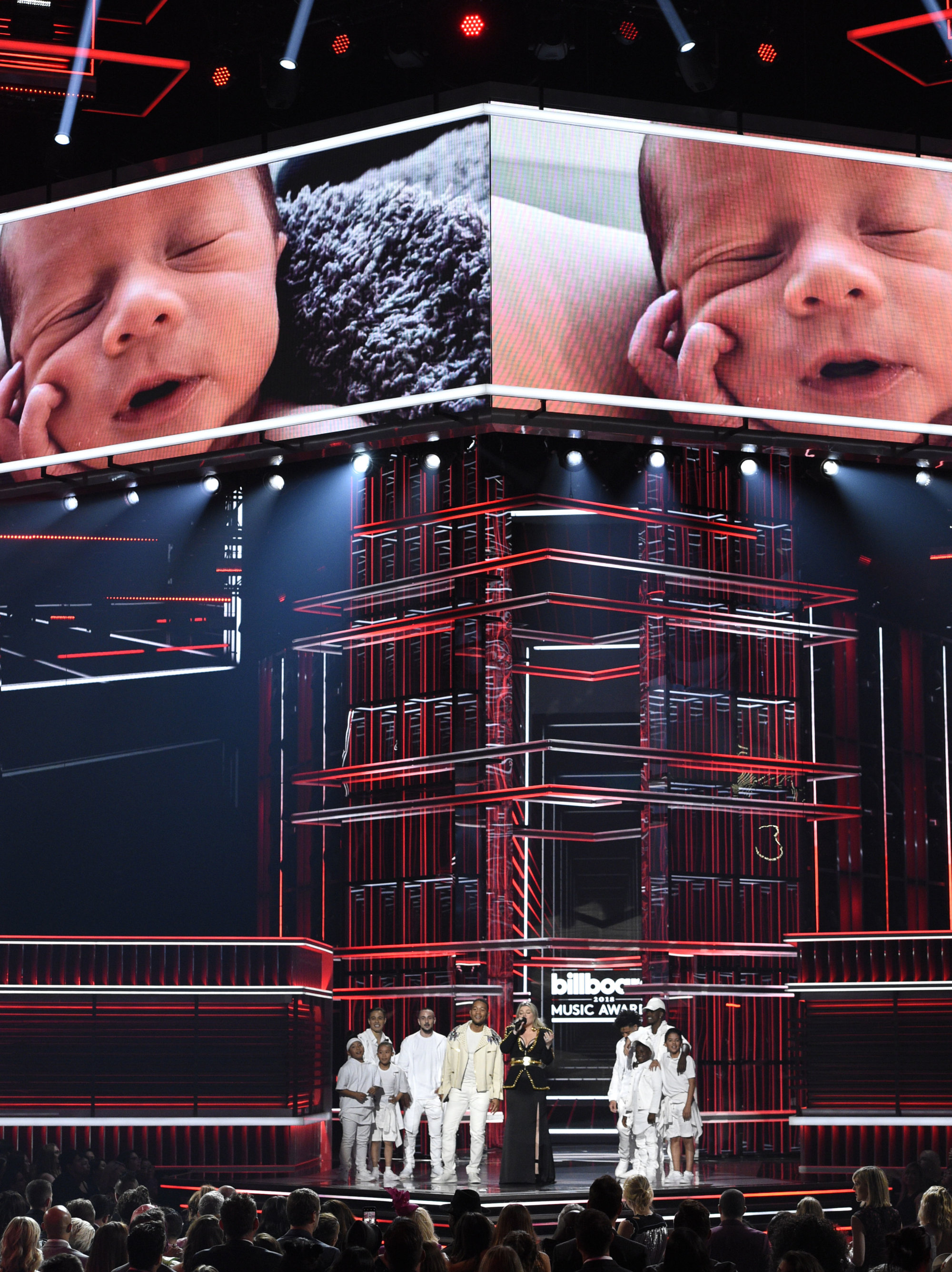 Host Kelly Clarkson congratulates John Legend on the birth of his son Miles Theodore, pictured on screen, at the Billboard Music Awards at the MGM Grand Garden Arena on Sunday, May 20, 2018, in Las Vegas. (Photo by Chris Pizzello/Invision/AP)