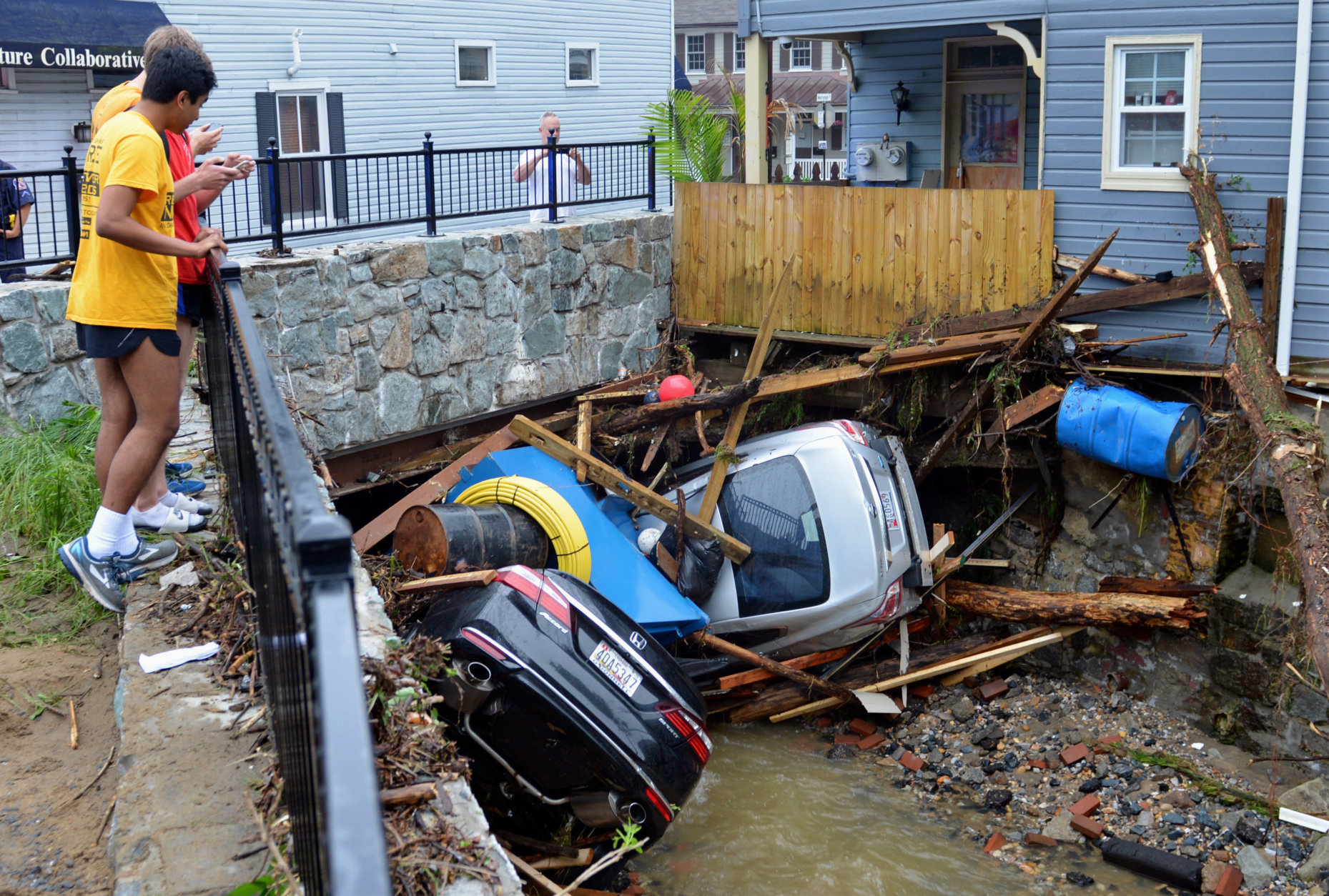 Residents gather by a bridge to look at cars left crumpled in one of the tributaries of the Patapsco River that burst its banks as it channeled through historic Main Street in Ellicott City, Md., on May 28, 2018.  (AP Photo/David McFadden. file)