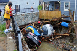 Residents gather by a bridge to look at cars left crumpled in one of the tributaries of the Patapsco River that burst its banks as it channeled through historic Main Street in Ellicott City, Md., Monday, May 28, 2018. Sunday's destructive flooding left the former mill town heartbroken as it had bounded back from another destructive storm less than two years ago. (AP Photo/David McFadden)