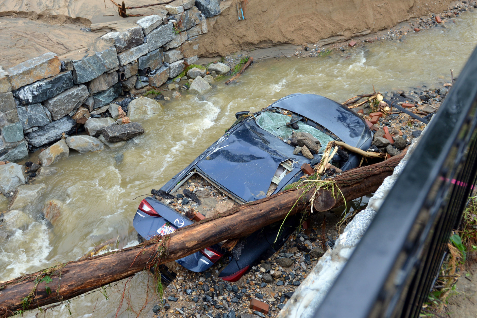Water moves past a car swept into the riverbank and smashed by a fallen tree is shown just off Main Street in flood-ravaged Ellicott City, Md., Monday, May 28, 2018. Sunday's destructive flooding left the former mill town heartbroken as it had bounded back from another destructive storm less than two years ago. (AP Photo/David McFadden)