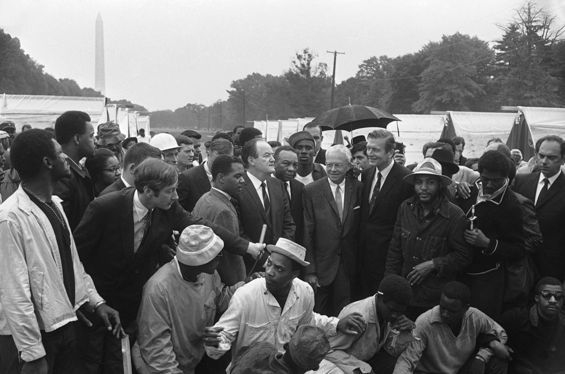Notables get a conducted tour of Resurrection City, the encampment erected by the Poor Peoples Campaign near the Washington Monument, left background, May 16, 1968. Identifiable at center of group, left to right are Rev. Walter Fauntroy, Wash. D.C. representative of Southern Christian Leadership Conference (left of handheld microphone); Vice President Hubert Humphrey; Mayor Walter Washington of Wash. D.C.; Mayor Ivan Allen Jr. of Atlanta; Mayor John Lindsay of New York City, and Rev. James Bevel of Southern Christian Leadership Conference. (AP Photo/John Rous)