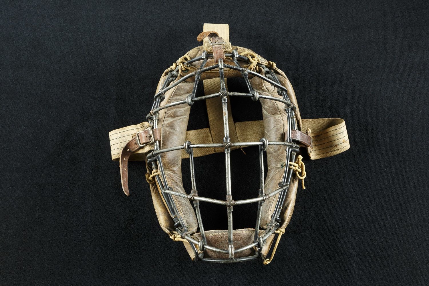 Early Catcher’s Mask 
With a well-earned fear of foul tips ricocheting off his head, Harvard’s Alexander Tyng wore a converted fencer’s mask for a game in 1877, becoming the first-known player to don a catcher’s mask. Only a year later, the patented headgear appeared in Spalding’s sporting goods catalog and professional catchers began wearing masks. Modest modifications followed, such as additional padding and buckled straps. Charles Arnold, a student at Phillips Academy and Yale, used this mask from 1905 to 1914.
Charles Arnold’s catcher’s mask, 1905. Canvas, leather, and metal. Courtesy of the National Baseball Hall of Fame and Museum (082.00.00)
