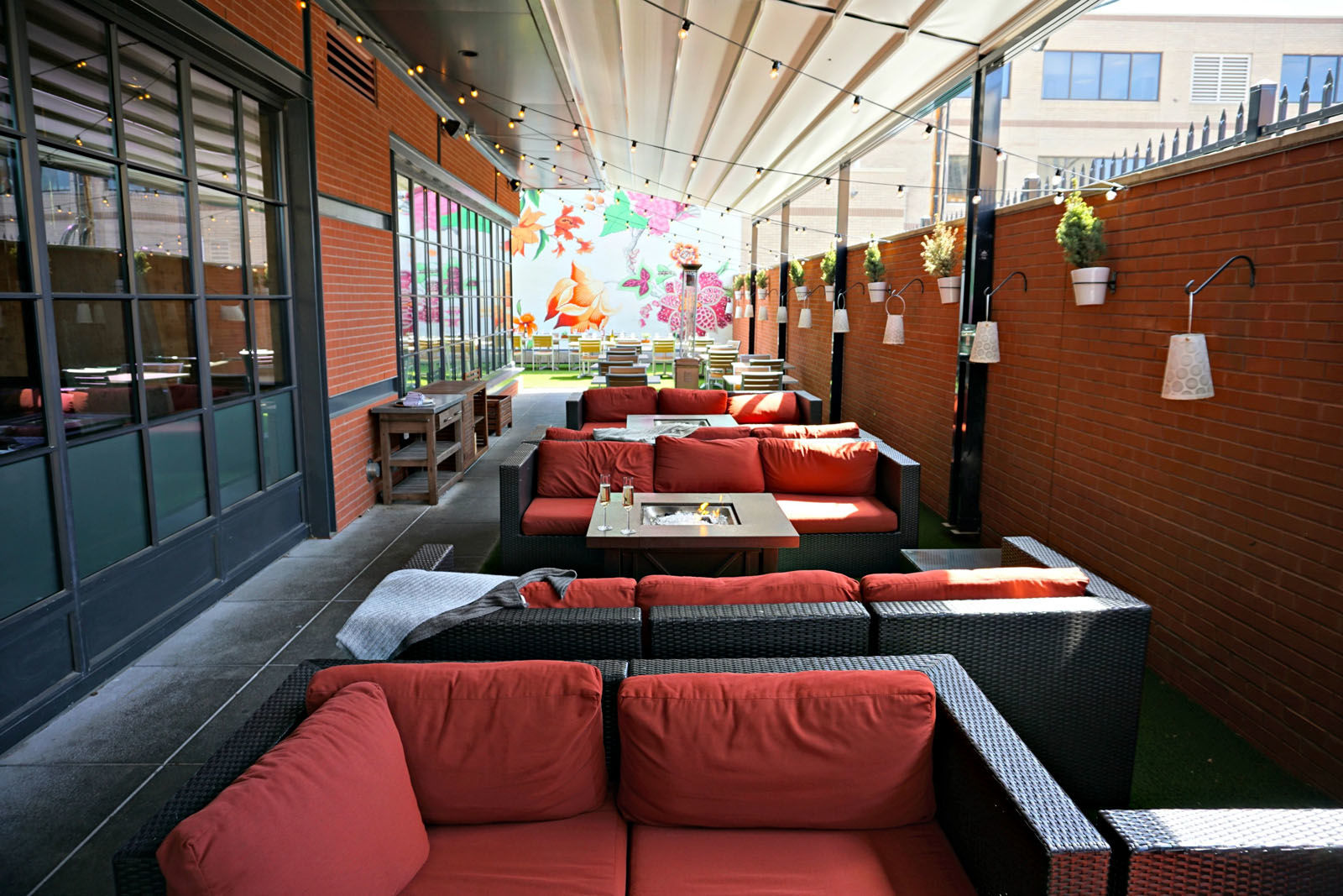 Hazel boasts a fun &amp; funky patio complete with astroturf, potted plant-lined brick walls, broad wicker seating, and fire pits to keep guests cozy in cooler temperatures. A bright, hand-painted floral mural serves as the centerpiece of the urban garden oasis. This summer, enjoy table side Spritz service via a roving cocktail cart. (Courtesy Hazel)