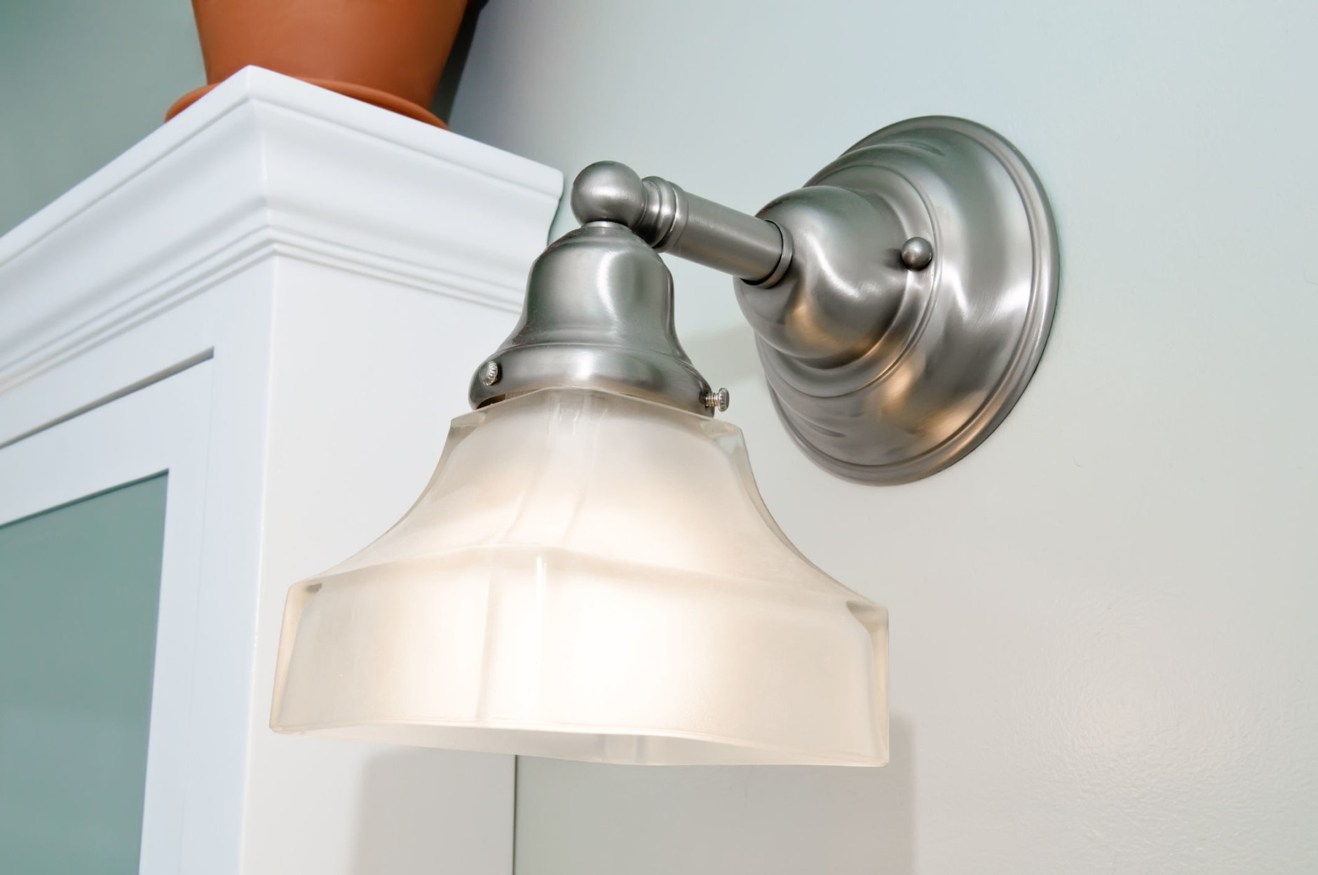 Closeup of a brushed nickel and frosted glass bathroom light fixture in a light blue bathroom.