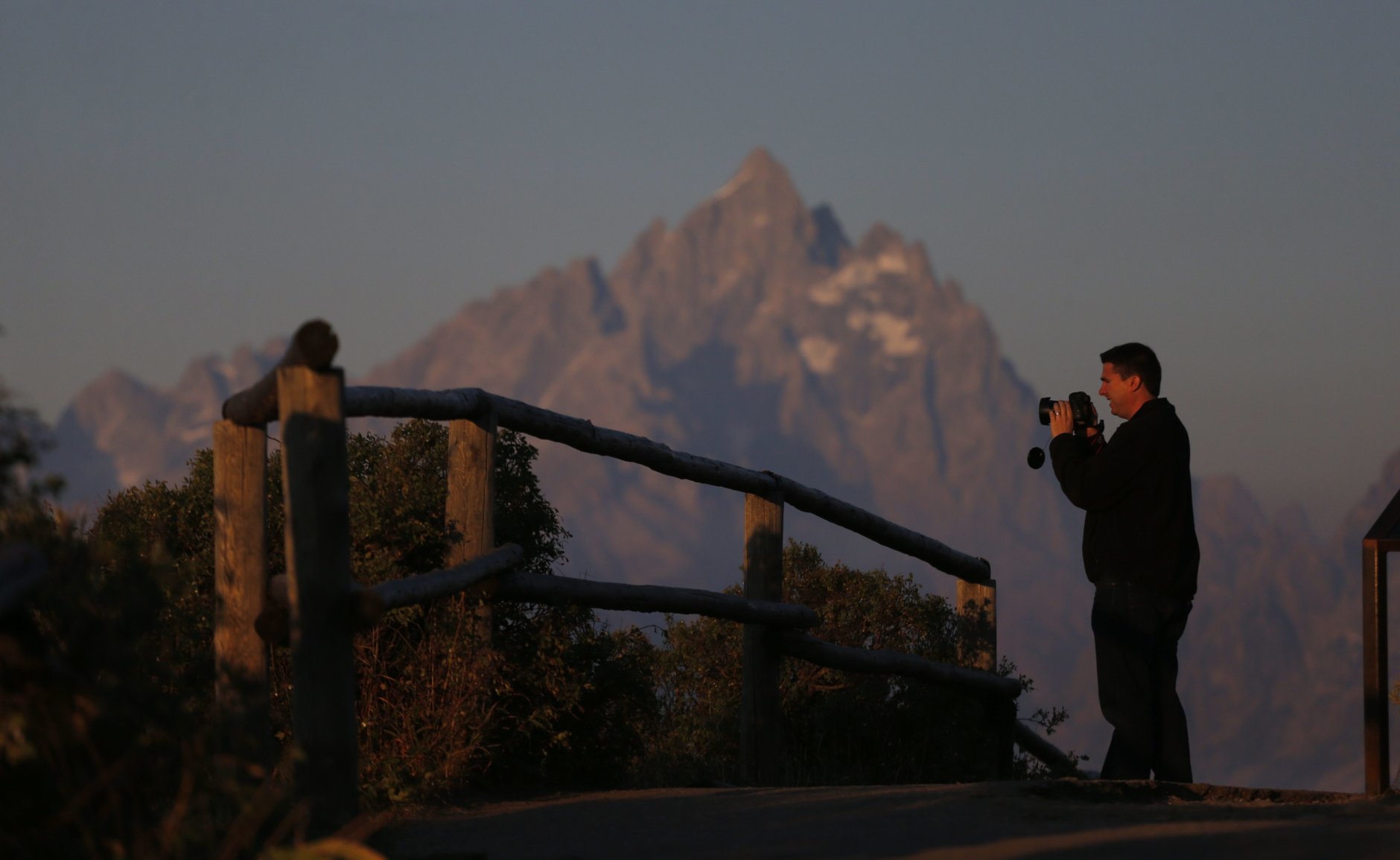 Park visitor Michael Quaide takes a picture as the sun at dawn illuminates mountain peaks, partially obscured by haze from the wildfires nearby as seen from Signal Mountain in Grand Teton National Park, Wyo., Aug 25, 2016. Aug 25, 2016 marked the 100th anniversary of the US National Park Service. (AP Photo/Brennan Linsley)
