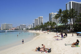 In this Monday, March 13, 2017 photo, people relax on the beach in Waikiki in Honolulu. Hawaii has filed a lawsuit challenging President Donald Trump's revised travel ban, saying the executive order could harm the state's strong tourist economy. (AP Photo/Caleb Jones)