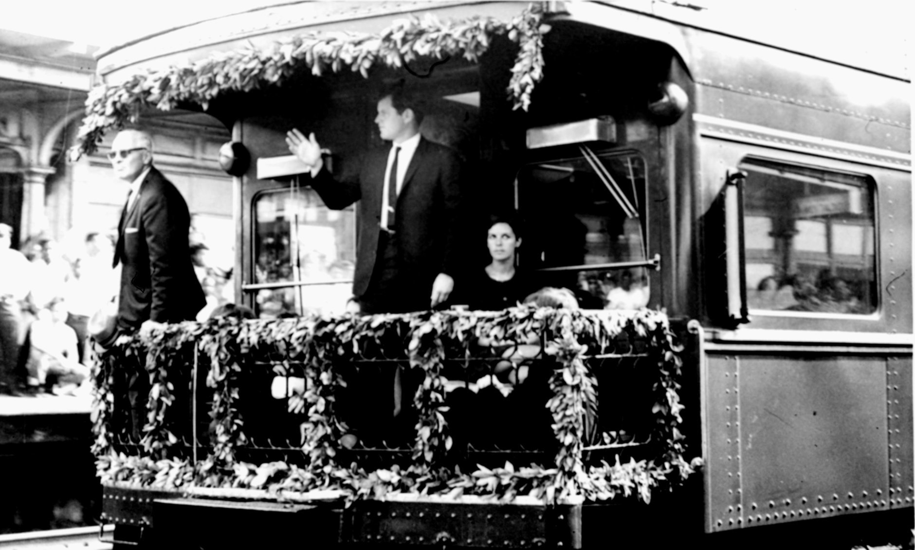 Sen. Edward M. Kennedy waves from the rear platform of the observation car bearing the remains of his slain brother, Sen. Robert F. Kennedy, as the funeral train passed through North Philadelphia Station, June 8, 1968.  Others on platform are unidentified.  (AP Photo)