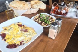 The breakfast spread at Fava Pot, including ful medames, basturma and eggs, and fresh-baked aish baladi. (WTOP/Noah Frank)