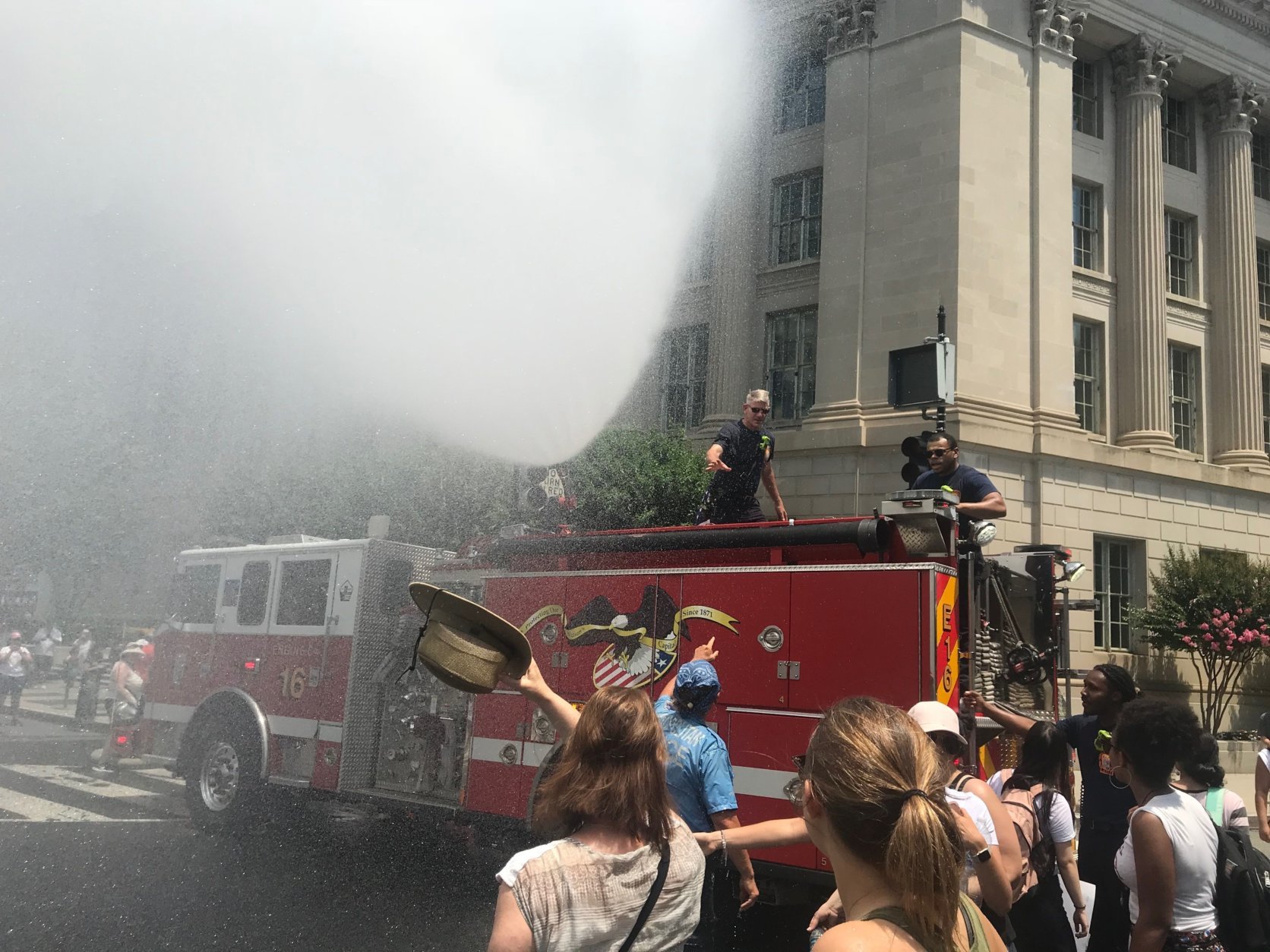 D.C. Fire Engine 16 tapped a fire hydrant at 16th and H Street Northwest, dispensing a spray of water over the intersection to provide demonstrators some relief from the heat. (WTOP/Dick Uliano)
