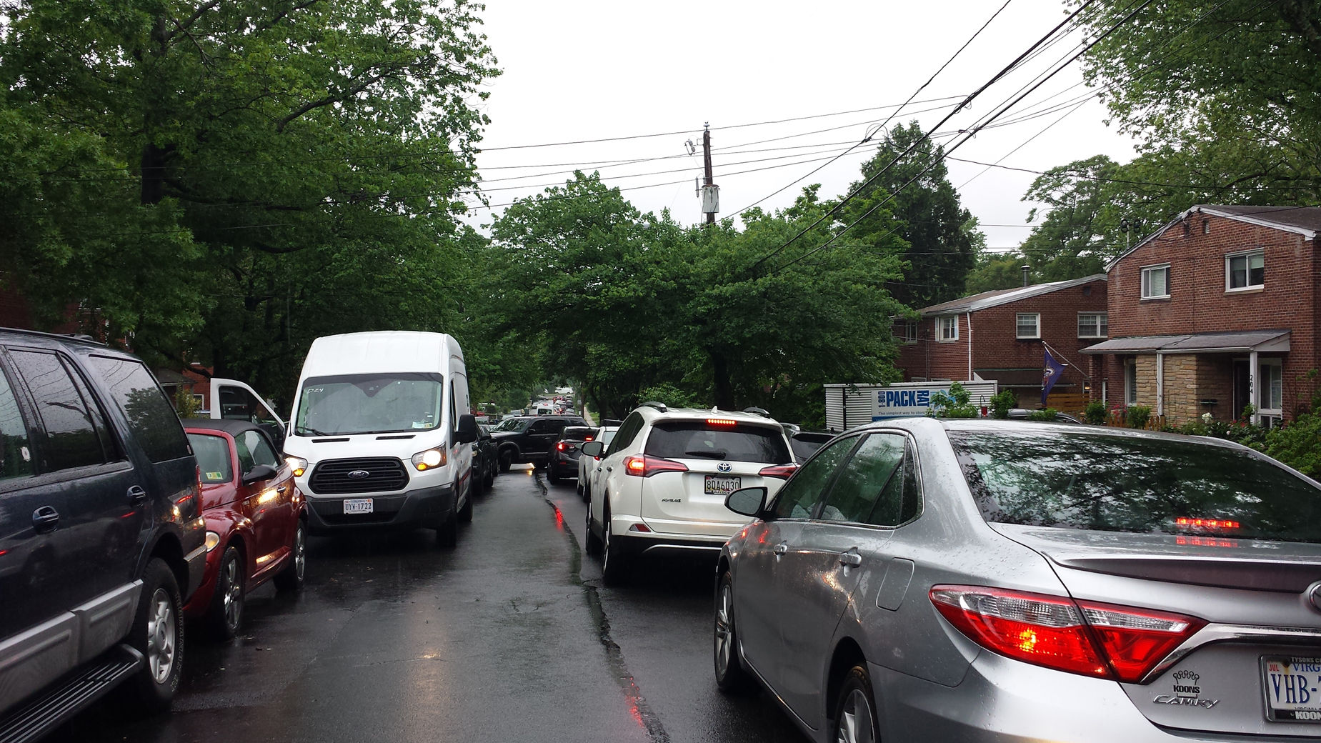 The cars on the right are parked on East Taylor Run Parkway, a two-way street that frequently gets backed up as drivers cut through the Alexandria neighborhood to get to Capital Beltway and southern Fairfax County. Drivers frequently block the street so that others coming the other way cannot use the road. This photo was taken on May 16, 2018. WTOP/Colleen Kelleher)