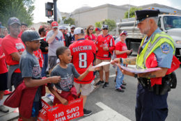 Washington Metropolitan Police Officer Robert T. Fennell, right, helps hand out posters to a pair of young fans before the start the Stanley Cup victory parade on Constitution Ave., along the National Mall. (AP Photo/Pablo Martinez Monsivais)