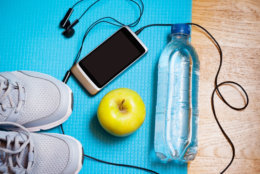 Sport equipment. Sneakers, water, apple, smartphone and earphones on yoga mat