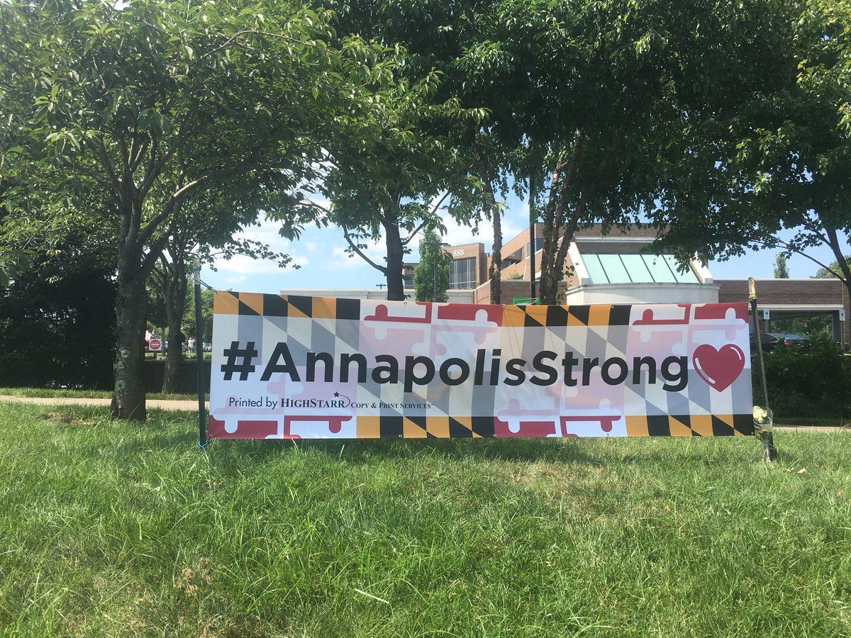 A banner is seen by a memorial near where five people were killed at the Capital Gazette in Annapolis. (WTOP/Mike Murillo)