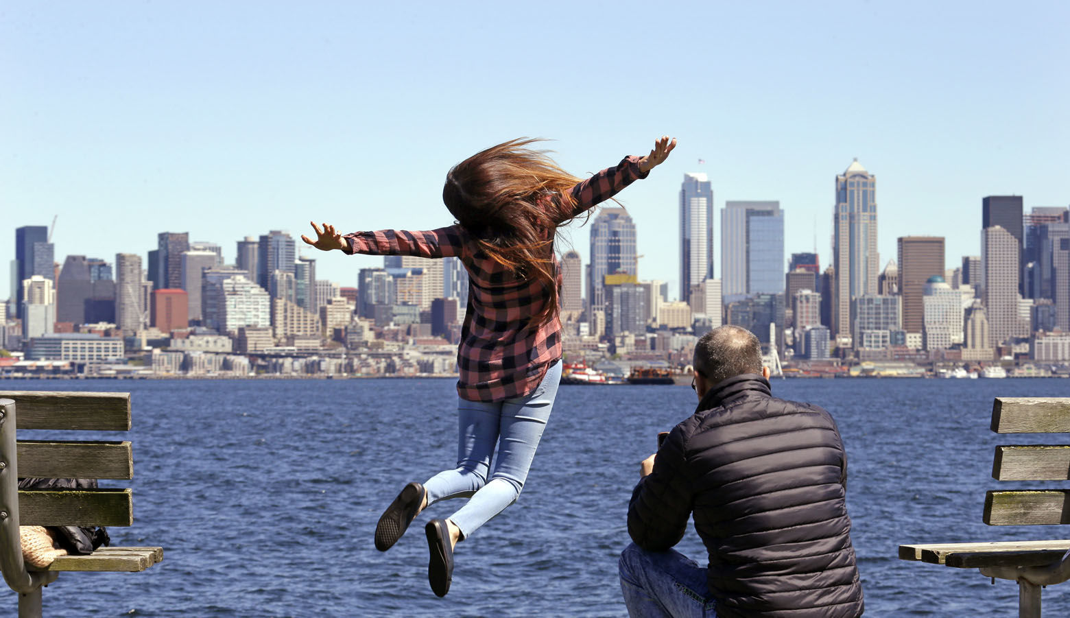 Mariel Toledo leaps for a photo taken by her friend Chi Nguyen in view of downtown Seattle on an unusually sunny day Friday, April 21, 2017. Rain is expected to return Saturday and continue for at least several days. (AP Photo/Elaine Thompson)