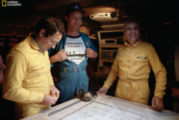 Titanic expedition members pore over blueprints of the R.M.S. Titanic.  A joint expedition by the Woods Hole Oceanographic Institution and the Institut Franca is de Recherches pour L'exploitation des Mers was formed to find the Titanic's final resting place.  The chief scientist of the Woods Hole contingent was Robert D. Ballard, here proudly displaying a commemorative expedition t-shirt. (Emory Kristof/National Geographic)