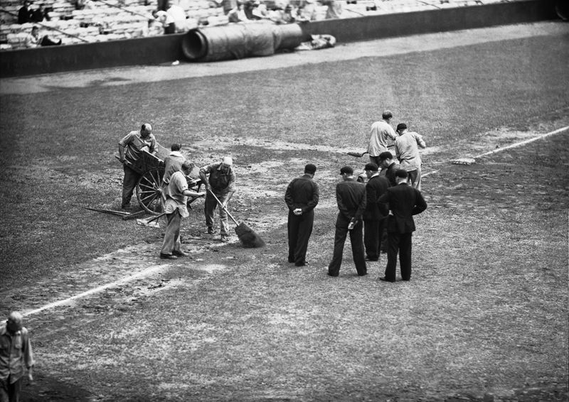 While grounds keepers spread dry dirt on Muddy Field in Shibe Park, on July 8, 1952 in Philadelphia, officiating umpires at all star game gather to decide on continuing or calling the game. The game was held up by continuous rain after five innings. (AP Photo)