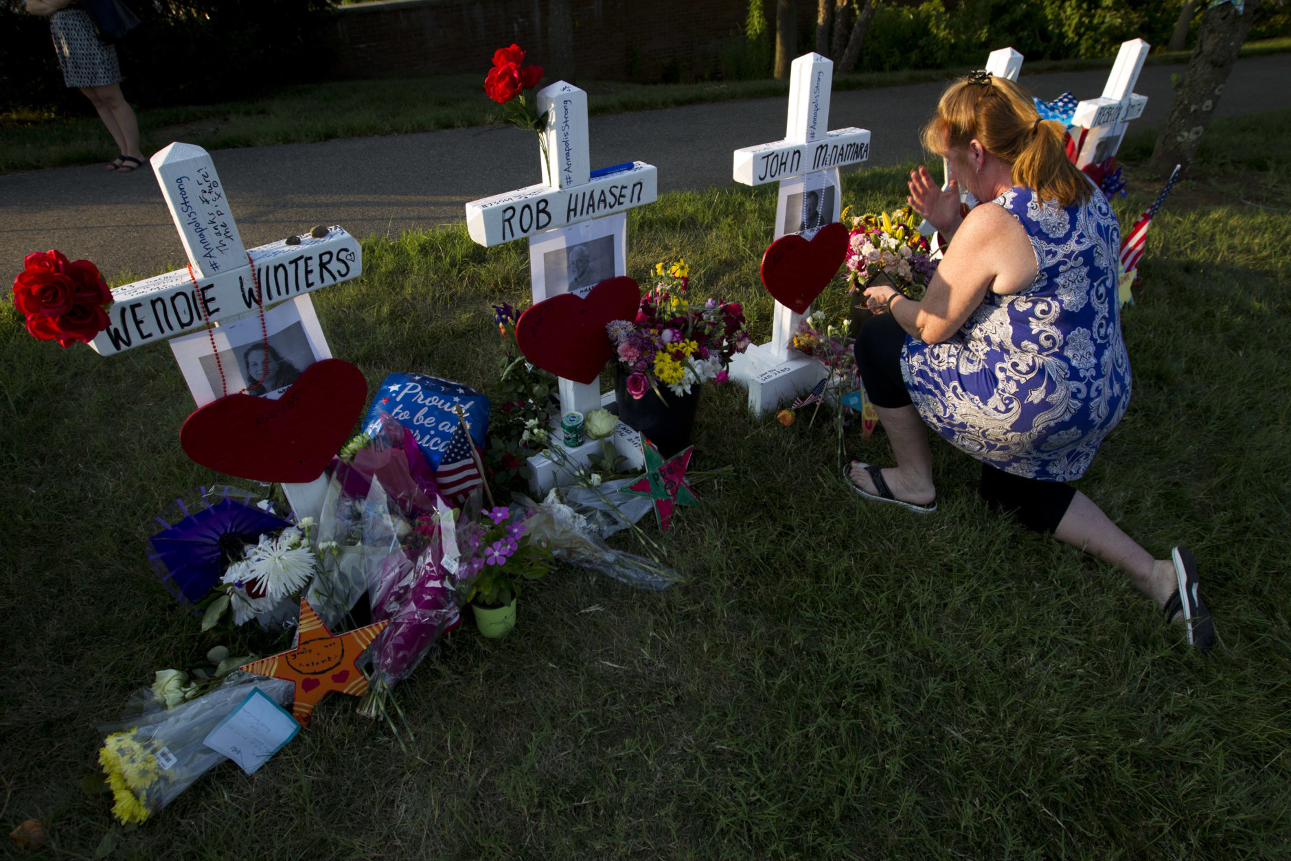 Colleen Joseph prays over the crosses at a makeshift memorial at the scene outside the office building housing The Capital Gazette newspaper in Annapolis, Md., on Sunday, July 1, 2018. Jarrod Ramos is charged with murder after police say he opened fire Thursday at the newspaper. (AP Photo/Jose Luis Magana)