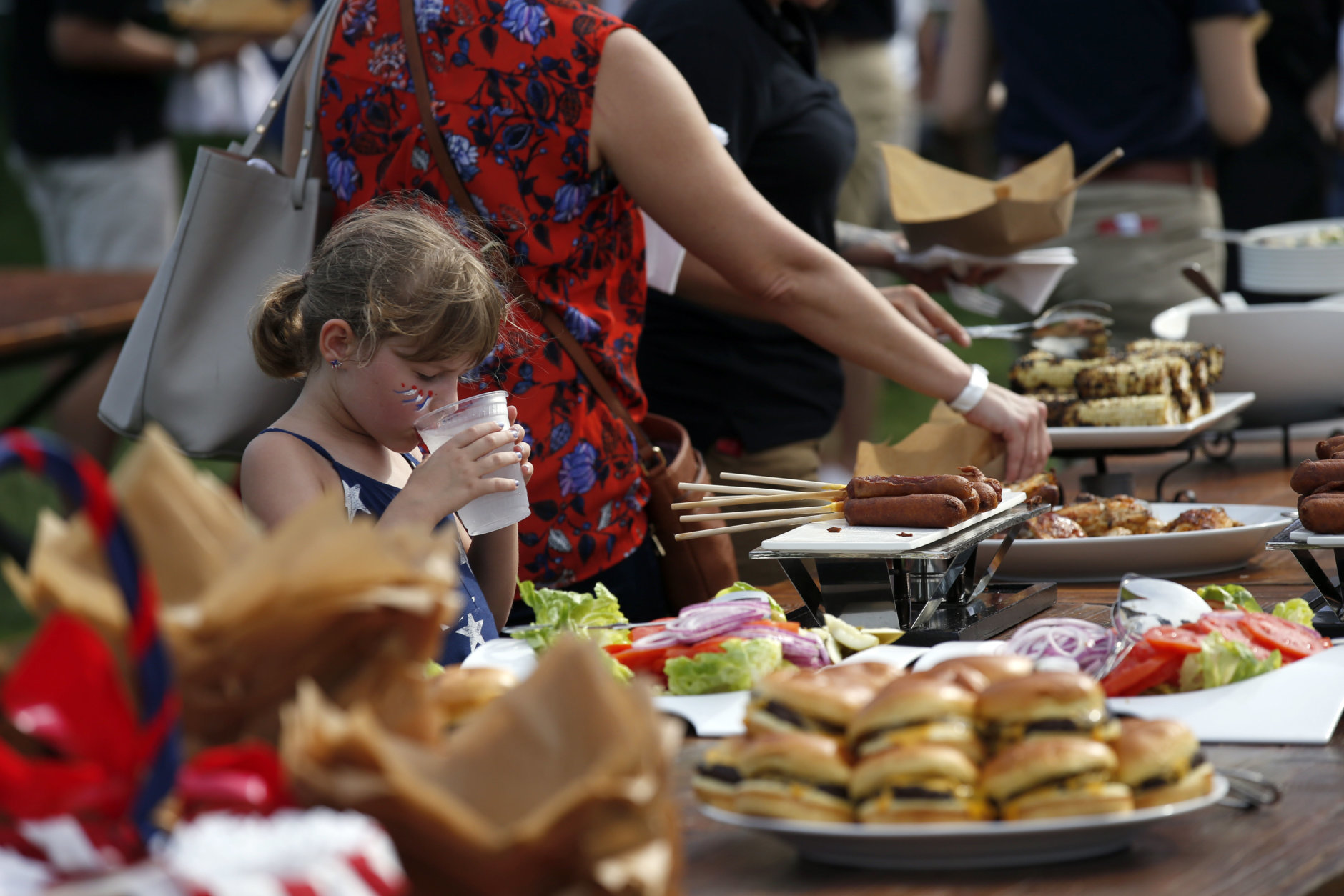 A child takes a drink in front of the food buffet during an afternoon picnic for military families on the South Lawn of the White House, Wednesday, July 4, 2018, in Washington. (AP Photo/Alex Brandon)