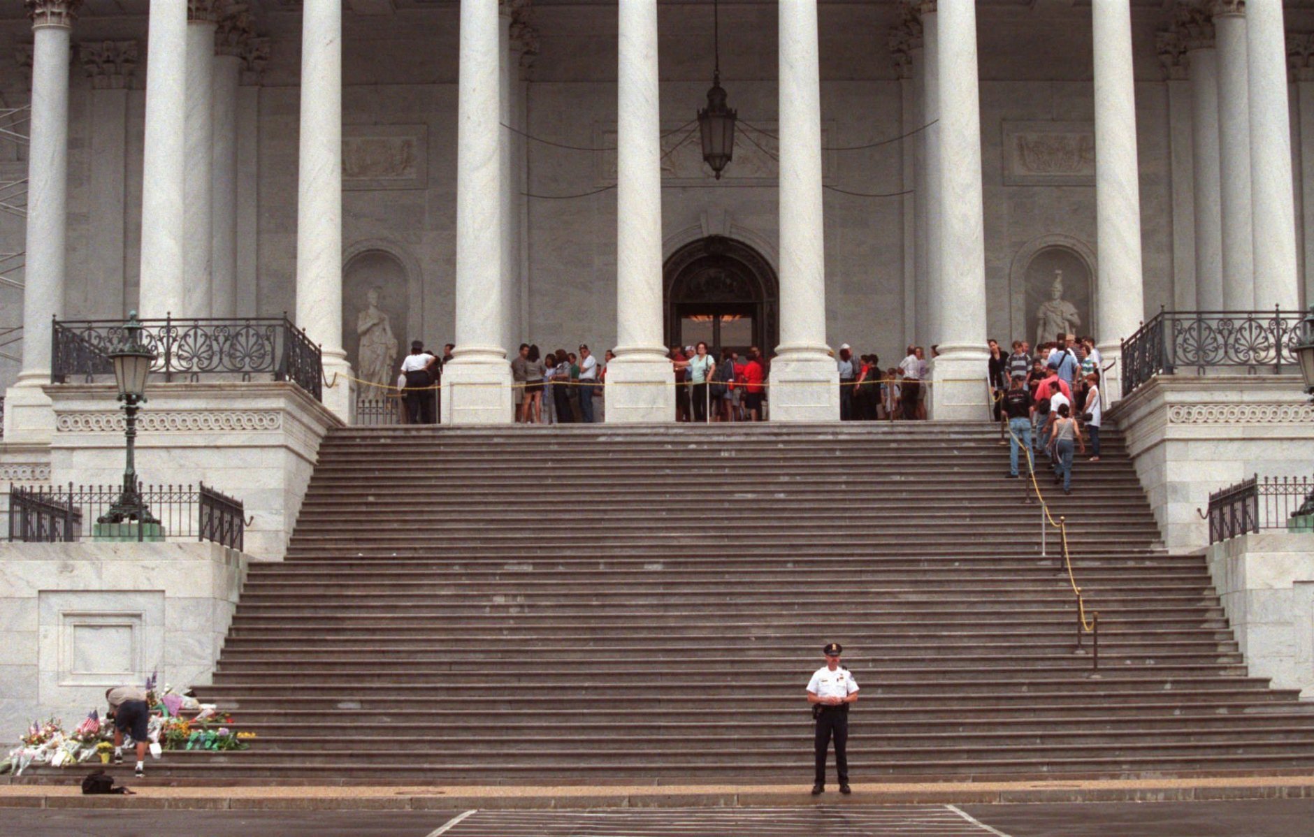 A Capitol Hill police officer stands watch in front of the U. S. Capitol Sunday, July 26, 1998 in Washington as visitors wait to enter the building.  Two officers were killed and a tourist wounded during a brief shooting spree in the building on Friday, July 24, 1998.  The tourist has been released from the hospital and the suspect in the shootings remains hospitalized in serious condition after being shot by police.   (AP Photo/Khue Bui)