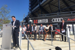Jason Levien speaks in front of Audi Field's northwest gate as D.C. players, sponsors, politicians and MLS leadership look on. (WTOP/Noah Frank)