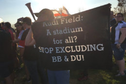 A protesters holds a sign outside Audi Field during D.C. United's first game in the new stadium. (WTOP/Liz Anderson)