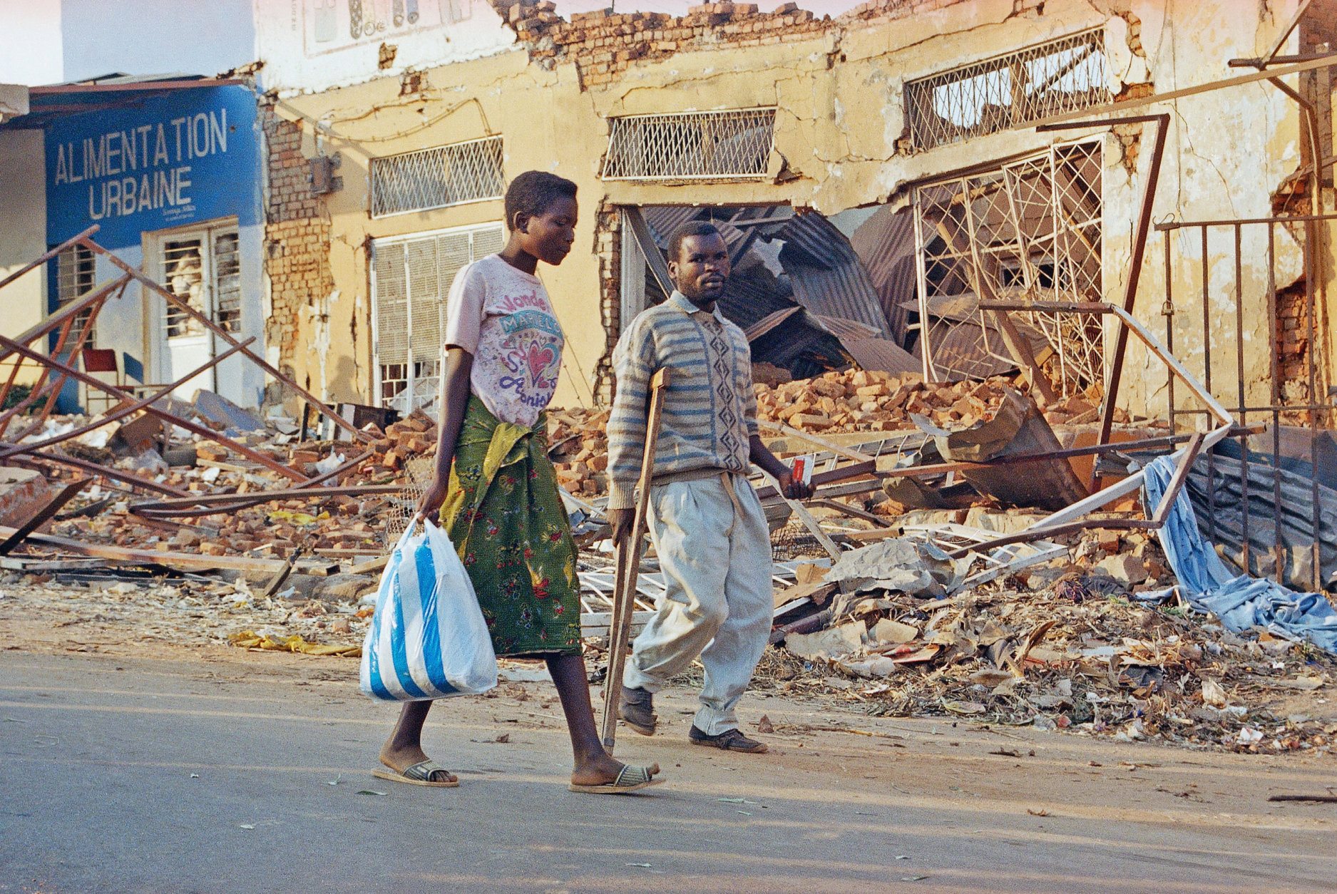 Kigali residents walk past debris in the city center, Wednesday, August 3, 1994. The U. S. Embassy reopened for the first time since a genocidal rampage caused most foreigners to leave nearly four months ago. The death of Rwanda's president in a mysterious plane crash touched off ethnic slaughter and reignited a civil war that together claimed 350,000 to 500,000 lives. Most of the dead were minority Tutsis slain by Hutu soldiers and militiamen. The victorious Tutsi-dominated rebels installed a new government July 18. (AP Photo/Dominic Cunningham-Reid)