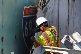 A DDOT contractor peels back a sheet of plywood, revealing an overhead sign pointing toward the never-built South Leg of the I-695 Inner Loop Freeway.  (WTOP/Dave Dildine)