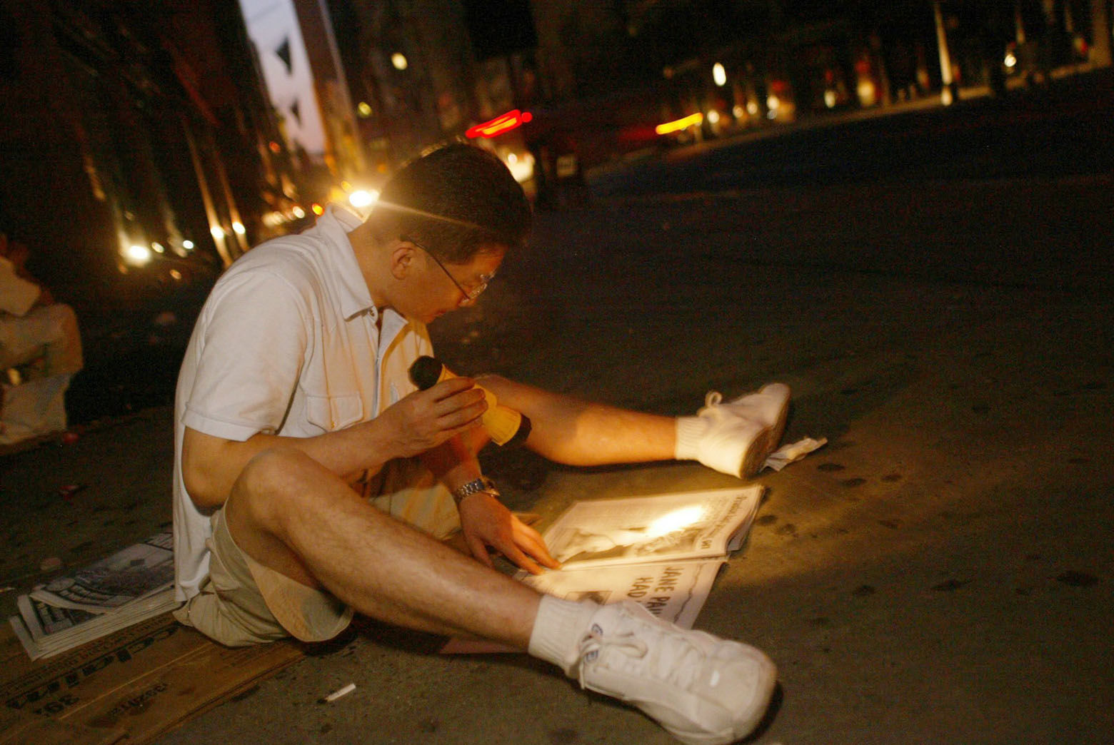 Joung Yun of Flushing, Queens, reads a newpaper by flashlight as he sits on the sidewalk at New York's Fifth Ave. early Friday morning Aug. 15, 2003. A power outage hit most of northeastern United States Thursday afternoon, leaving the city in the dark. (AP Photo/Joe Kohen)