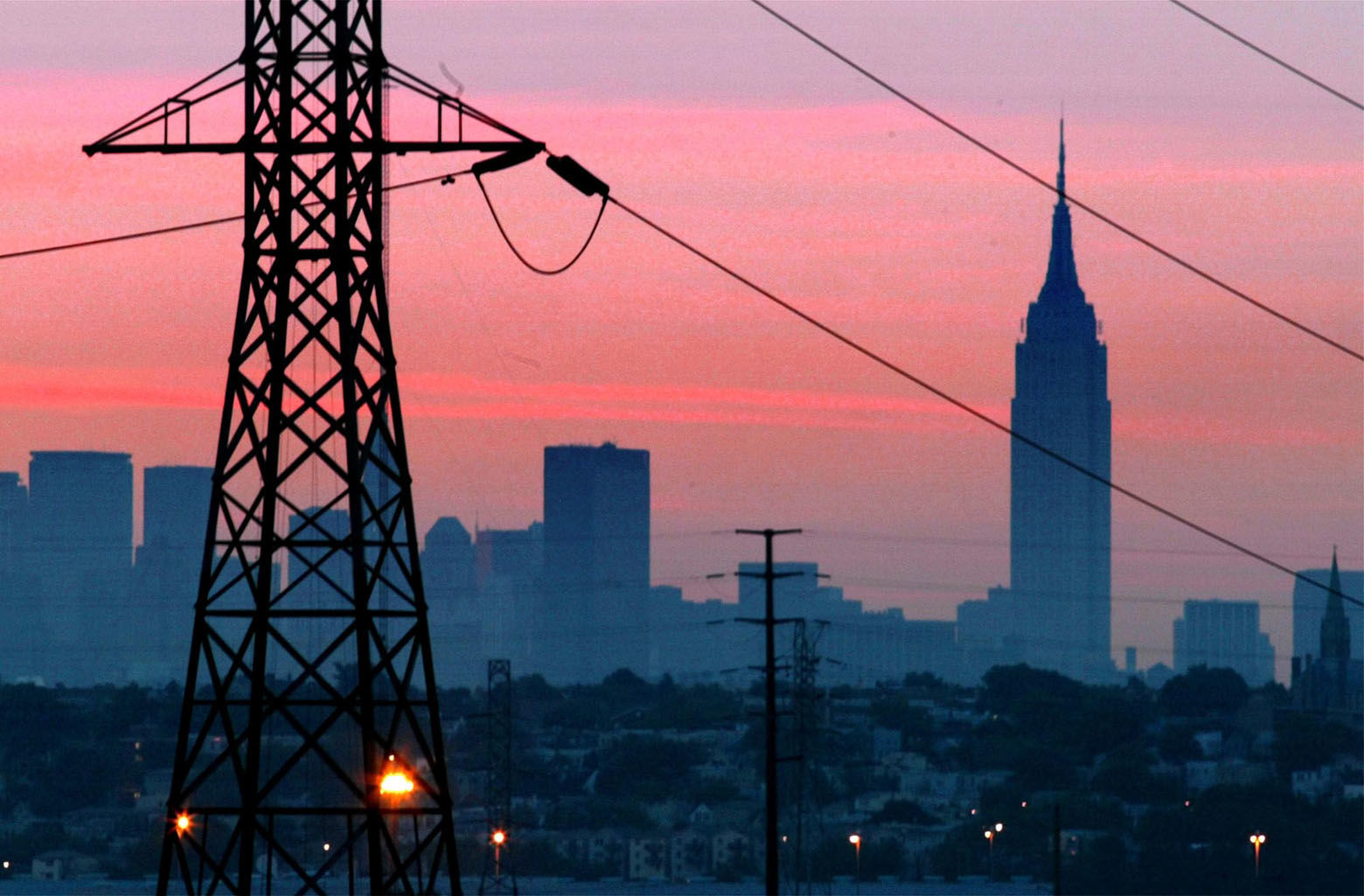 A darkened New York City is visible just before dawn through power lines from Jersey City, N.J., shown in foreground, with some lights visible, Friday, Aug. 15, 2003. The Empire State Building is in background.  (AP Photo/George Widman)