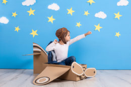 Little child girl in a pilot's costume is playing and dreaming of flying over the clouds. Portrait of funny kid on a background of bright blue wall with yellow stars and white clouds