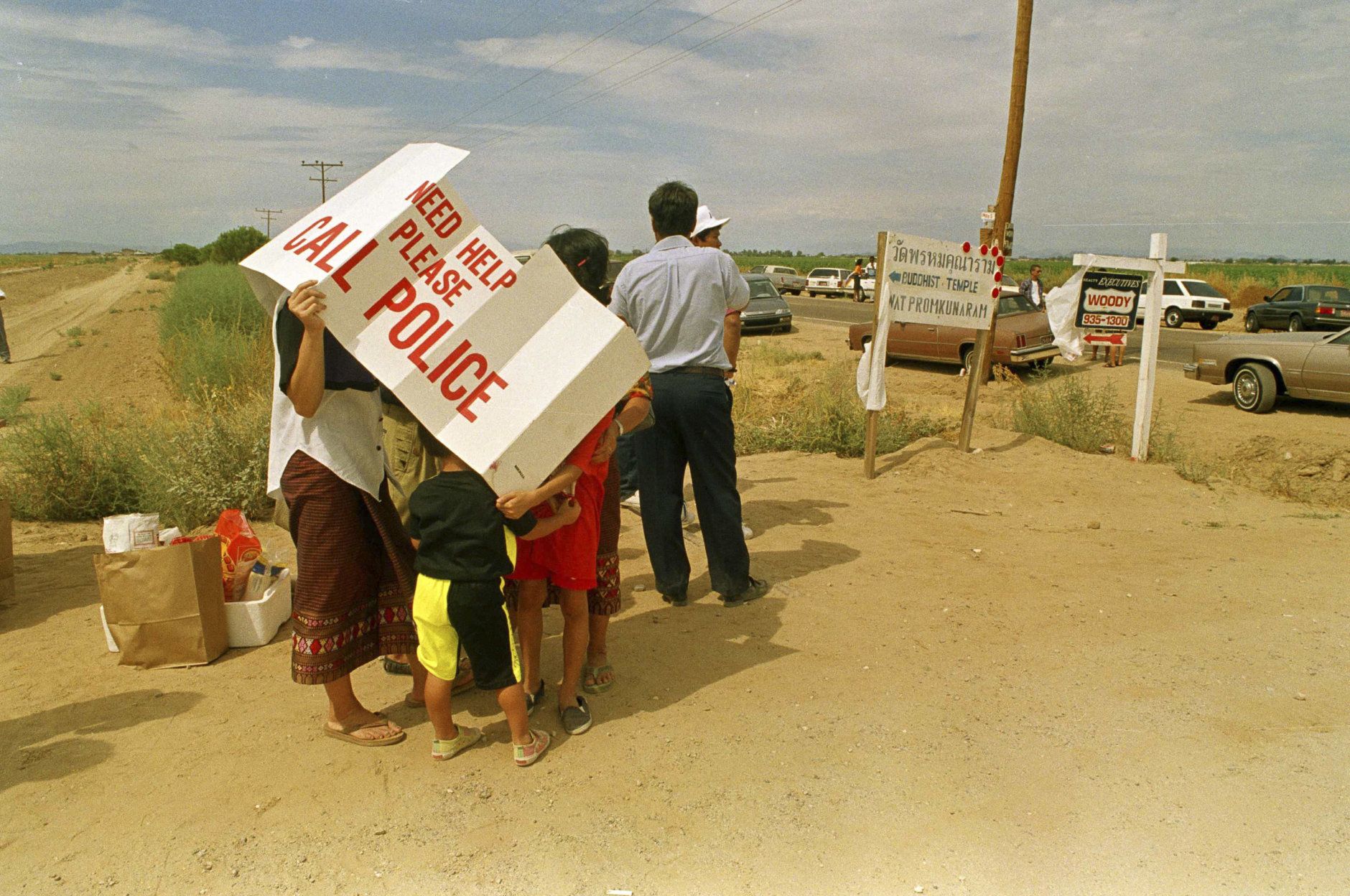 Trying to avoid the 100+ degree heat, a group of people hide under a windshield sun shade in west Phoenix, Arizona on August 10, 1991, hoping to receive word about nine people who were found slain at a Buddhist temple. Seven of those killed were Buddhist monks. (AP Photo/Scott Troganos)